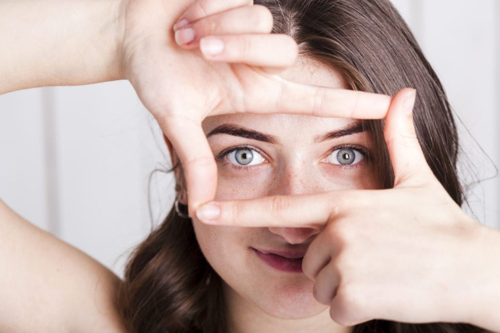 Bright-eyed woman framing her eyes with her hands