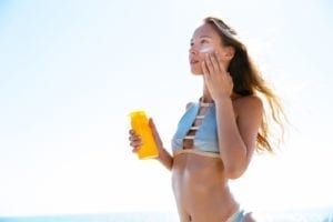 Woman applying sunscreen to face on beach.